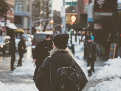 白天，背着背包的女人站在街上的雪地旁